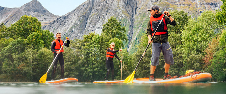 Drei Personen beim Stand-up-Paddeling in klarem Wasser, umgeben von Bergen und grüner Natur.