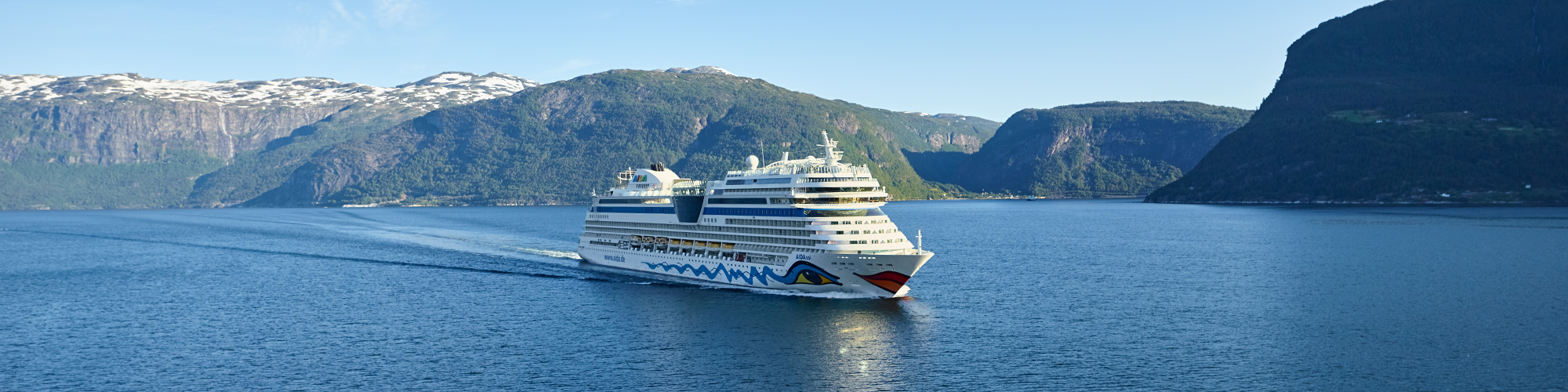 AIDAsol fährt auf den Betrachter zu, bei sonnigem Wetter auf dem blauen Meer in den Fjörden von Norwegen.