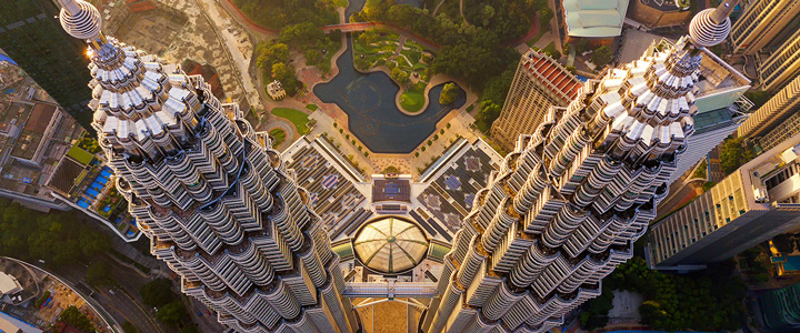 Die Petronas Twin Towers in Kuala Lumpur ragen neben dem grünen Park in die Höhe, moderne Architektur trifft auf ruhige Grünflächen.